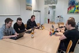 Ein Gruppe Menschen sitzt am Tisch und tauscht sich über Computer aus